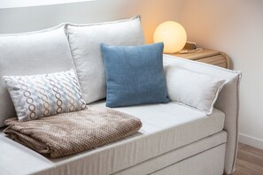 A sofa with patterned cushions, a throw blanket, and a bedside table with a lamp.