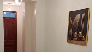 A hallway with a ceiling light fixture, a potted plant, a door, and a refrigerator.