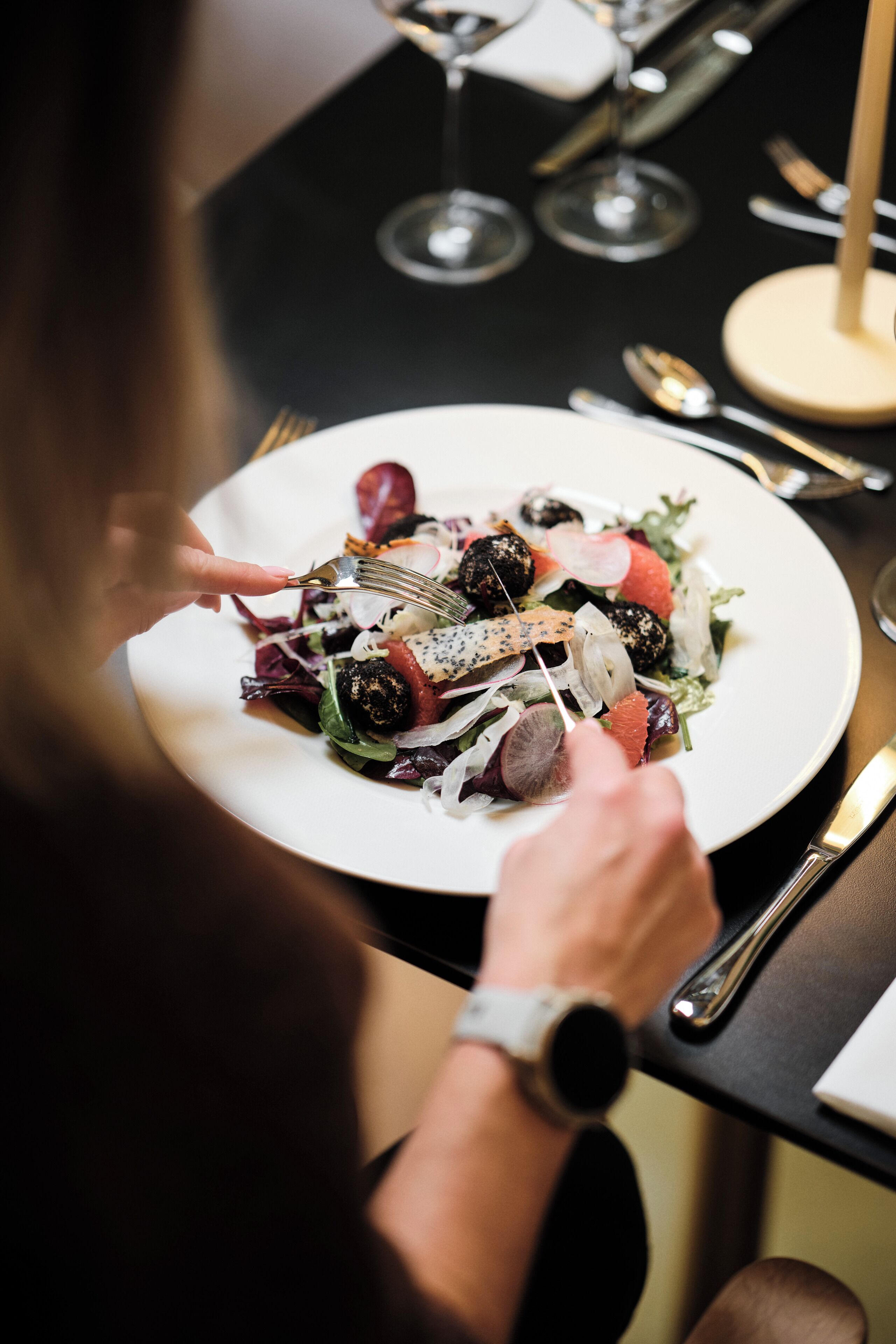 A person dining at a table with a plate of food, a fork, and a knife.