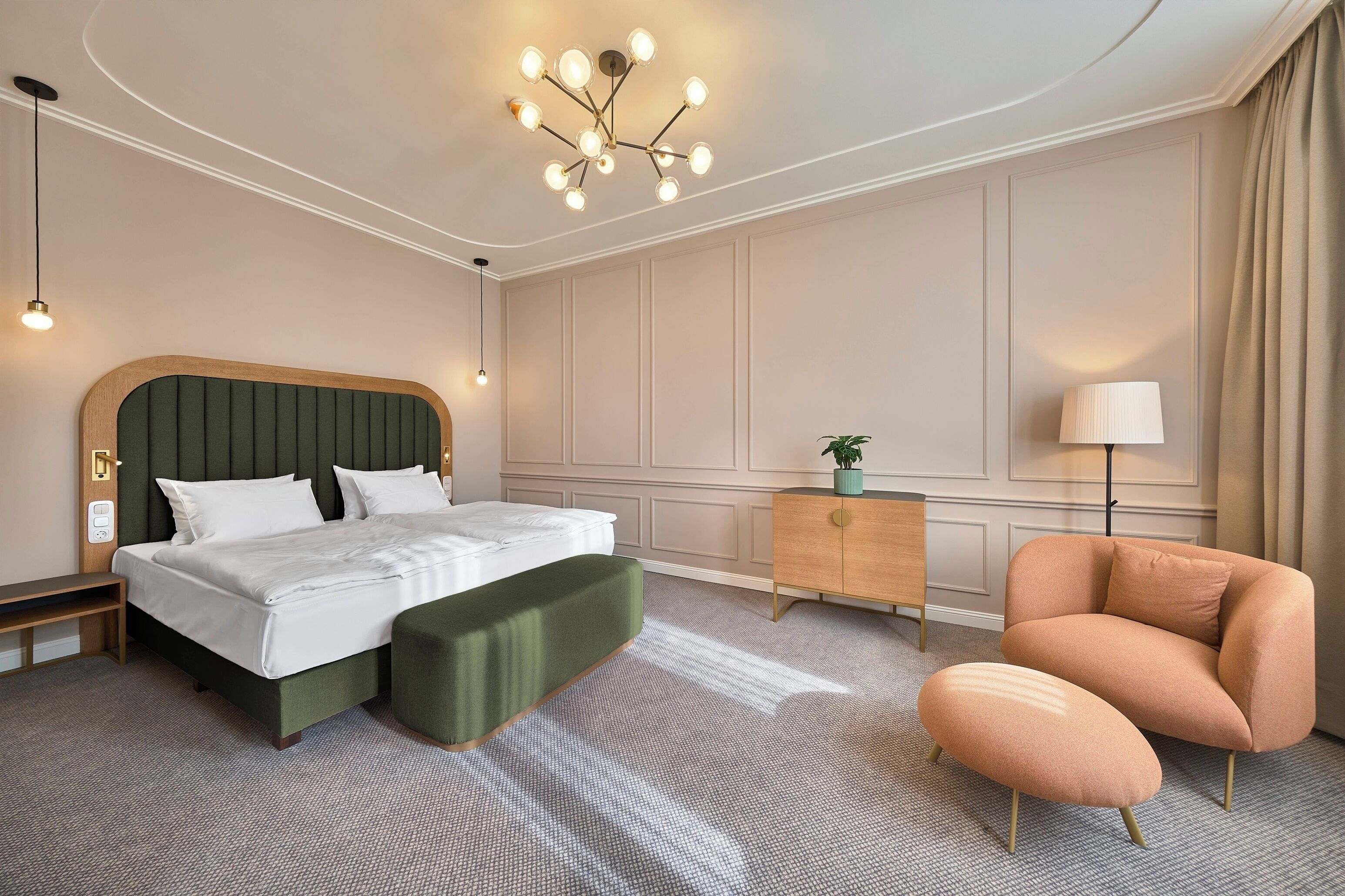 A hotel room with a bed, a green upholstered bench, a wooden nightstand, a lamp, and a chair.