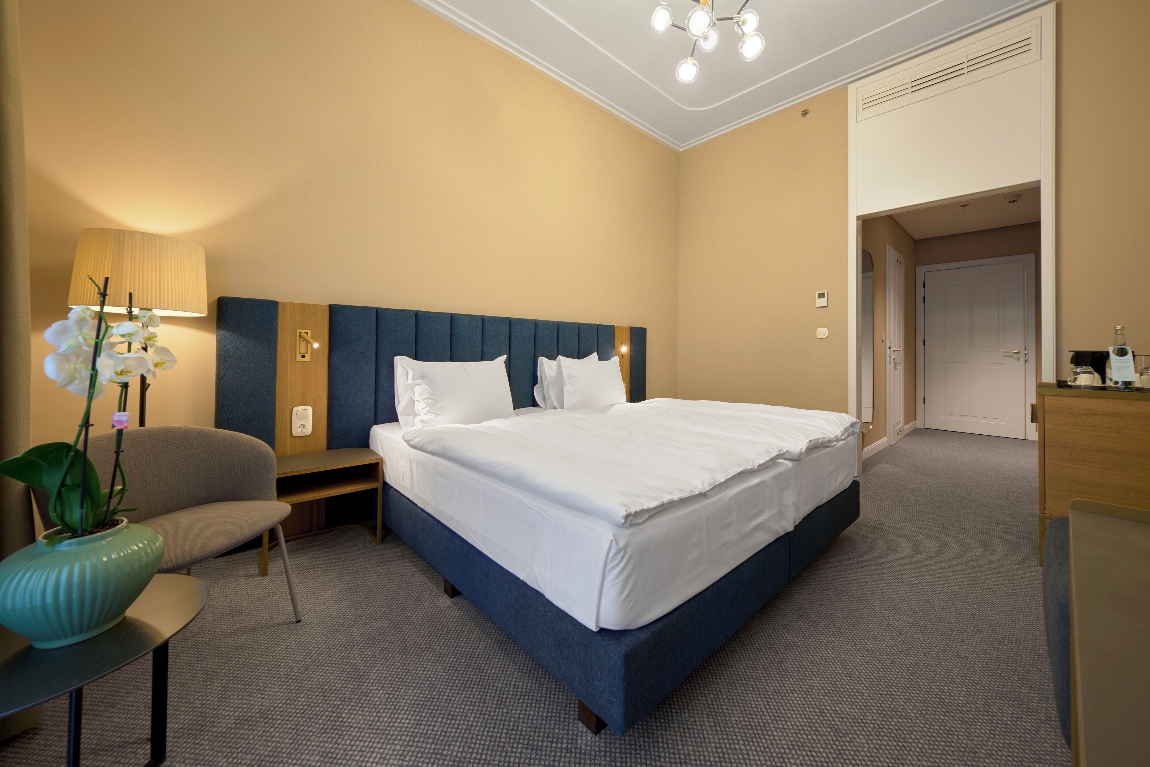 A hotel room with a large bed, a desk, a chair, and a potted plant.