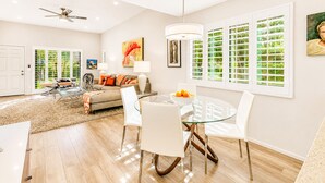 Un salon moderne avec une table à manger en verre, des chaises blanches, un canapé et un ventilateur de plafond.