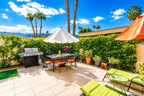 An outdoor patio with a grill, dining table, chairs, and umbrellas.