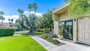 Une maison moderne avec une pelouse bien entretenue, des palmiers et un grand cactus dans le jardin.