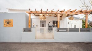 A building with a wooden pergola entrance, a sign reading "Platanos House Salacos," and a white exterior wall.
