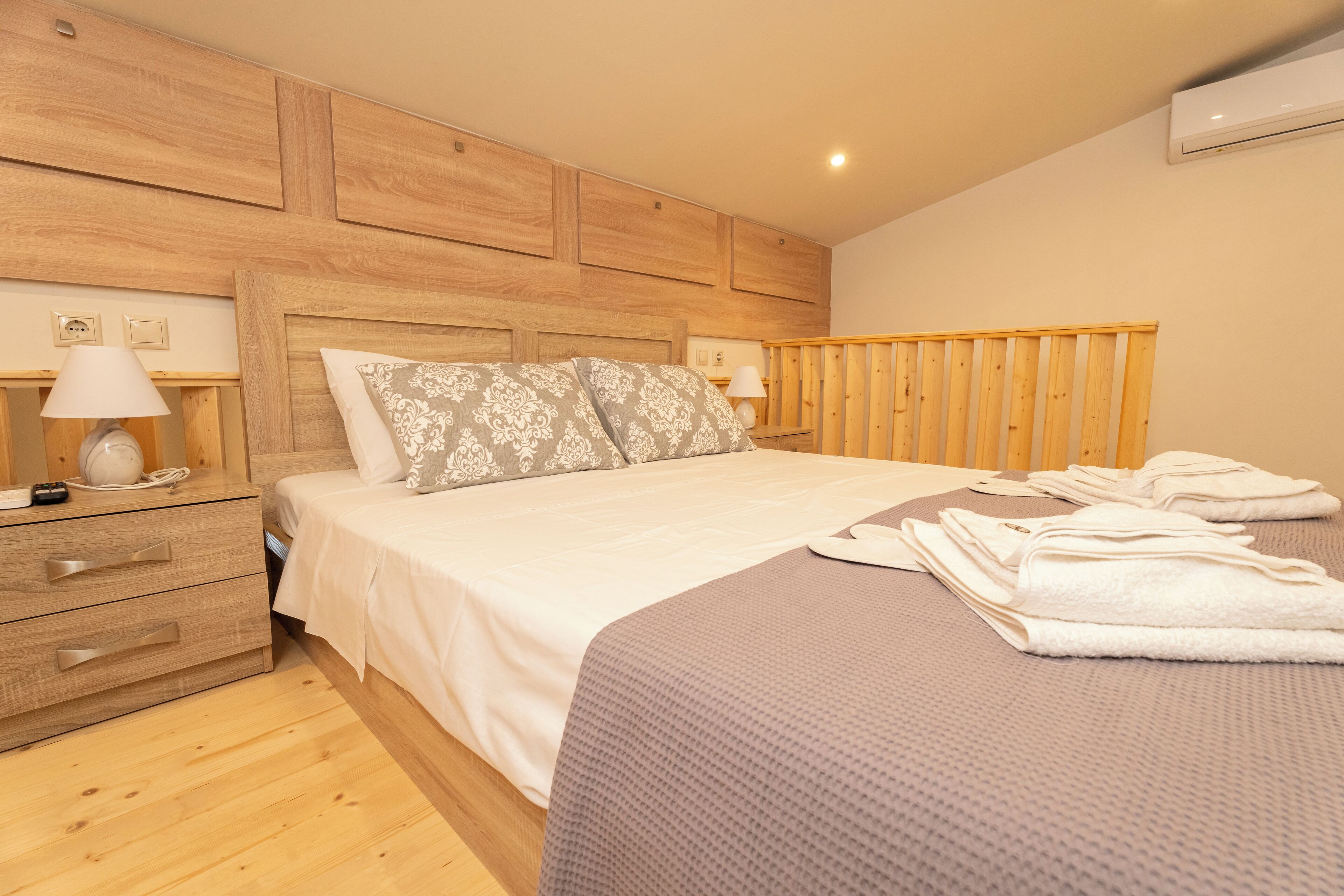 A bedroom with a wooden headboard, a bed with a patterned pillow, a bedside table with a lamp, and a folded towel on the bed.
