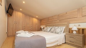 A bedroom with a bed, wooden wardrobe, bedside tables, and a TV mounted on the wall.