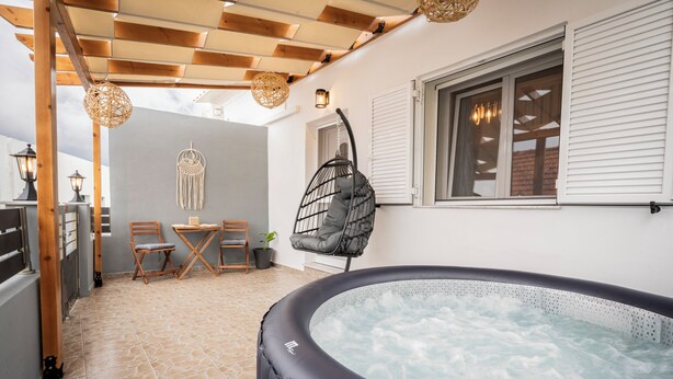 A hot tub in a covered outdoor area with a wooden ceiling, a table with chairs, and a wall-mounted dreamcatcher.