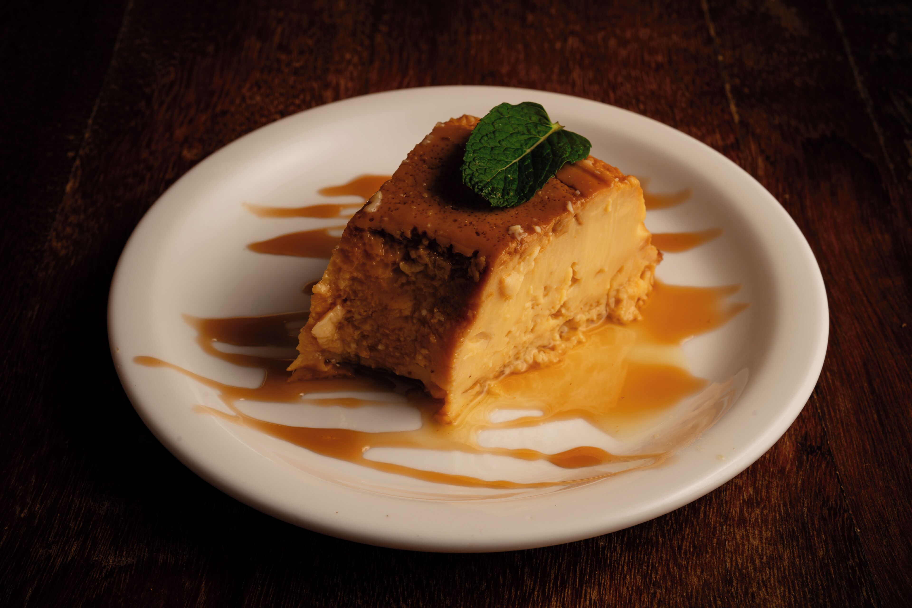 A dessert on a white plate with caramel sauce and a mint leaf garnish.
