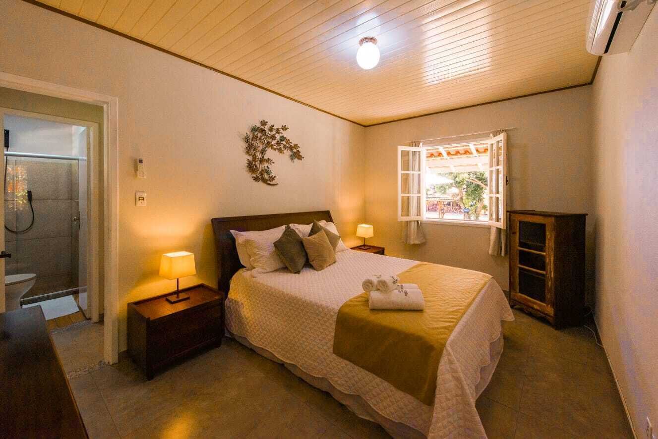 A bedroom with a bed, bedside lamps, a wooden headboard, a window with a view, and a door leading to a bathroom.