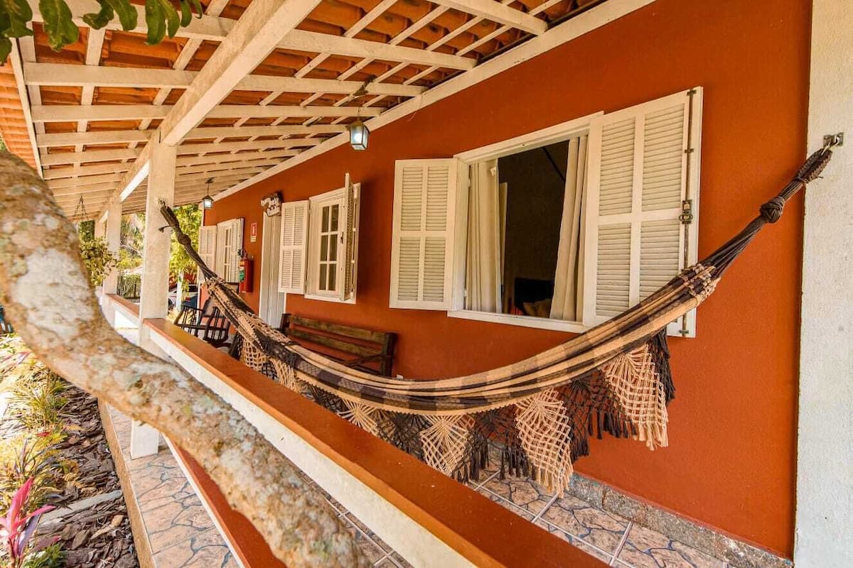 Un hamac sous une pergola en bois, un banc et un mur avec des volets.