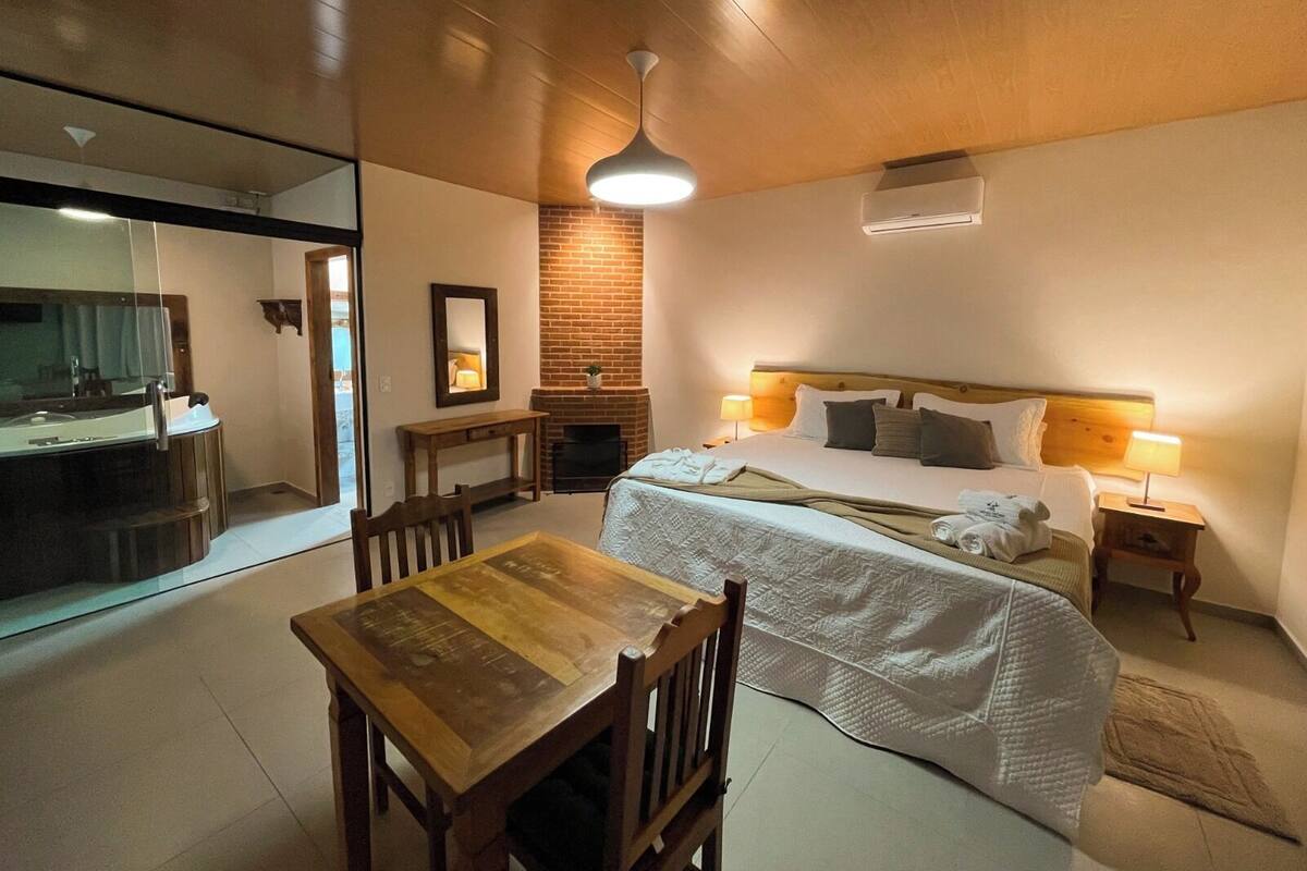 Une chambre d’hôtel moderne avec un plafond en bois, un grand lit avec une literie blanche, une petite table avec des chaises, une cheminée et un grand miroir.
