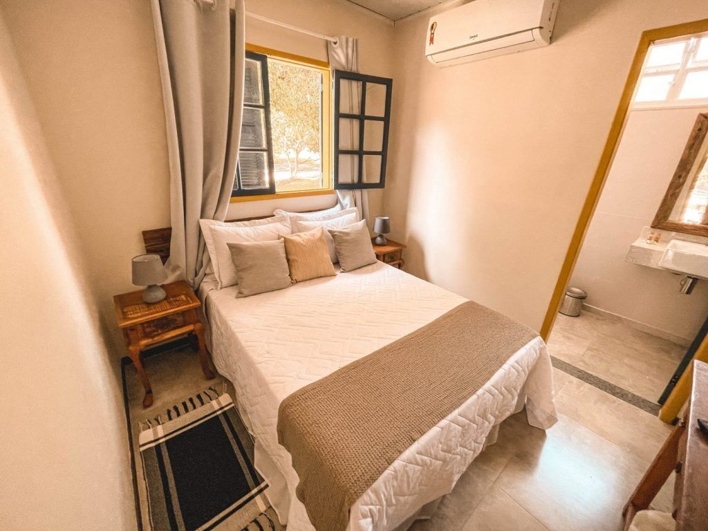 Un dormitorio con una cama, una mesita de noche, una lámpara, una ventana con cortinas y un equipo de aire acondicionado.