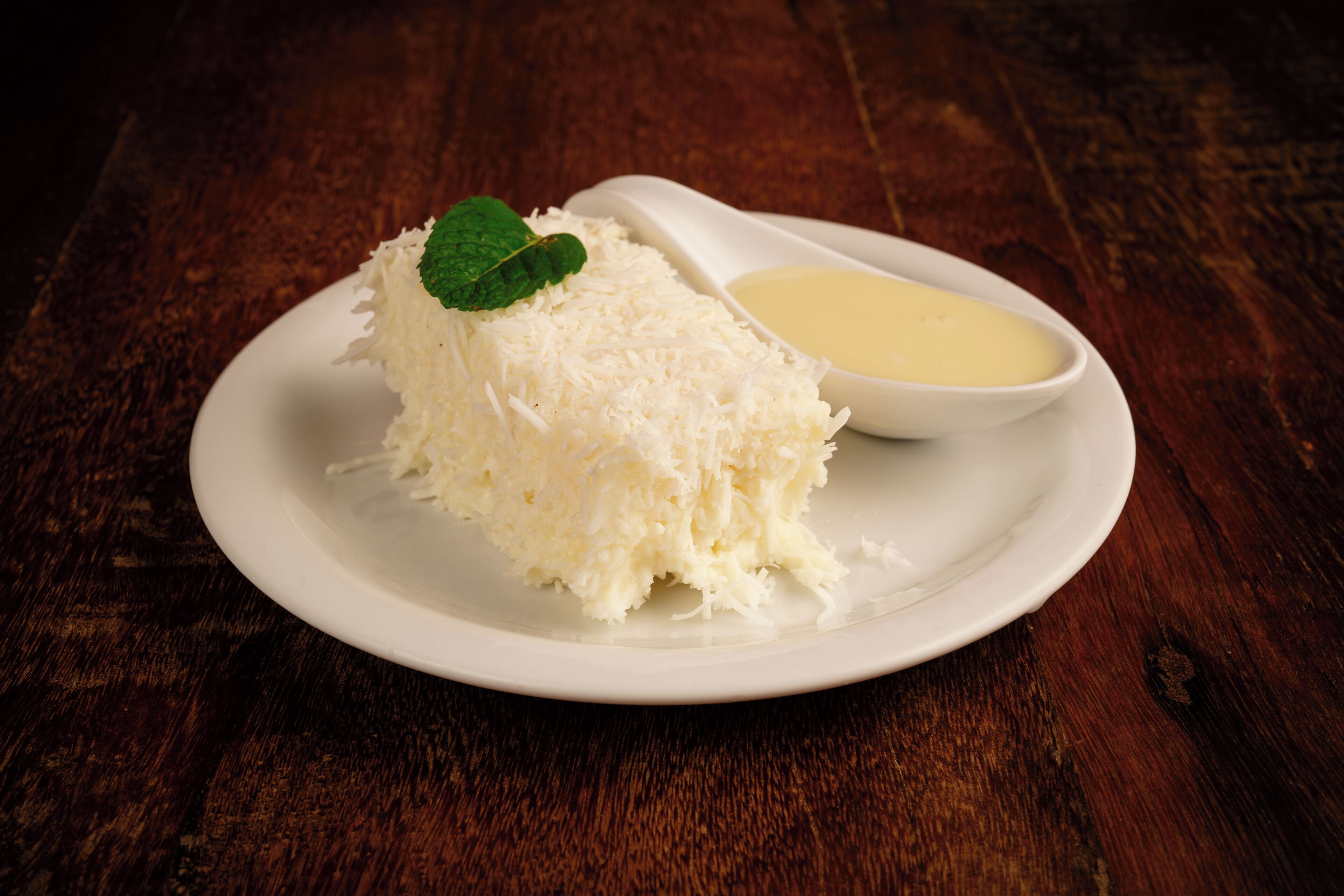 Un plato blanco con coco rallado y un recipiente pequeño de salsa sobre una mesa de madera.