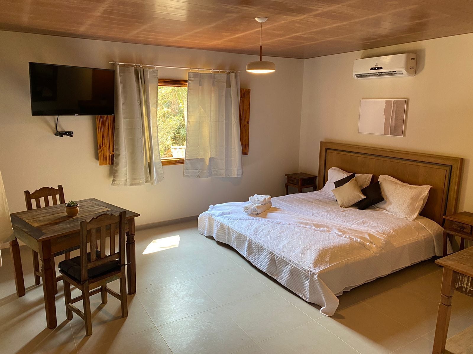A bedroom with a bed, a TV, a desk, and a window with curtains.