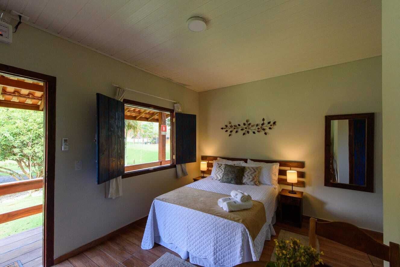 Un dormitorio con cama, mesita de noche, ventana con contraventanas y espejo adosado a la pared.