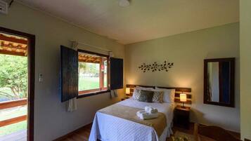 Un dormitorio con cama, mesita de noche, ventana con contraventanas y espejo adosado a la pared.