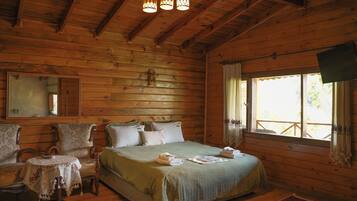 A wooden cabin bedroom with a bed, a small table, a mirror, and a window.