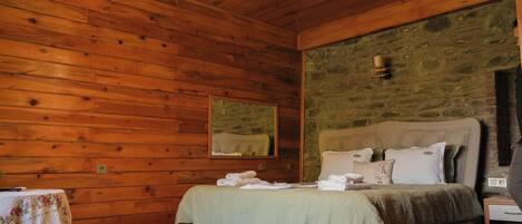 Una habitación con paneles de madera, una cama, una mesa con mantel floral y una pared de piedra.