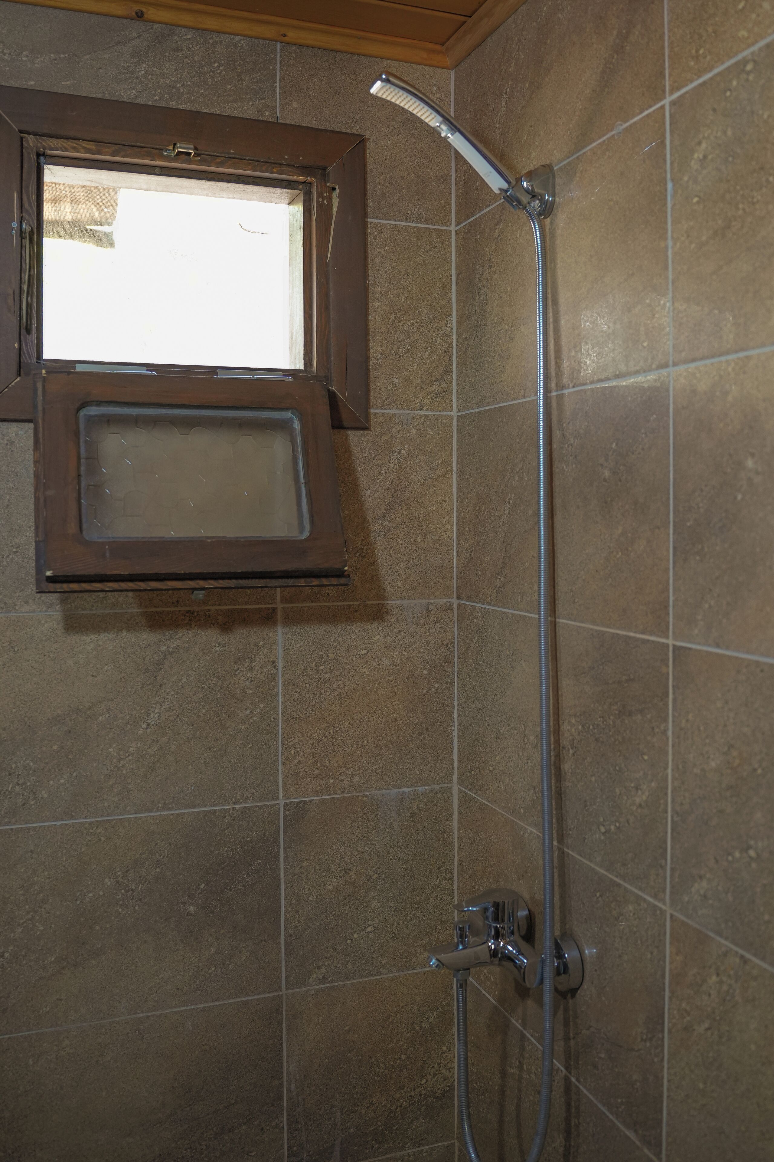 A shower with a window above it, tiled walls, and a visible showerhead.