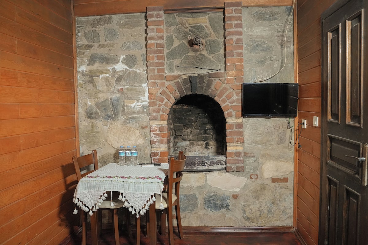 A rustic room with a stone fireplace, wooden walls, and a table with chairs.