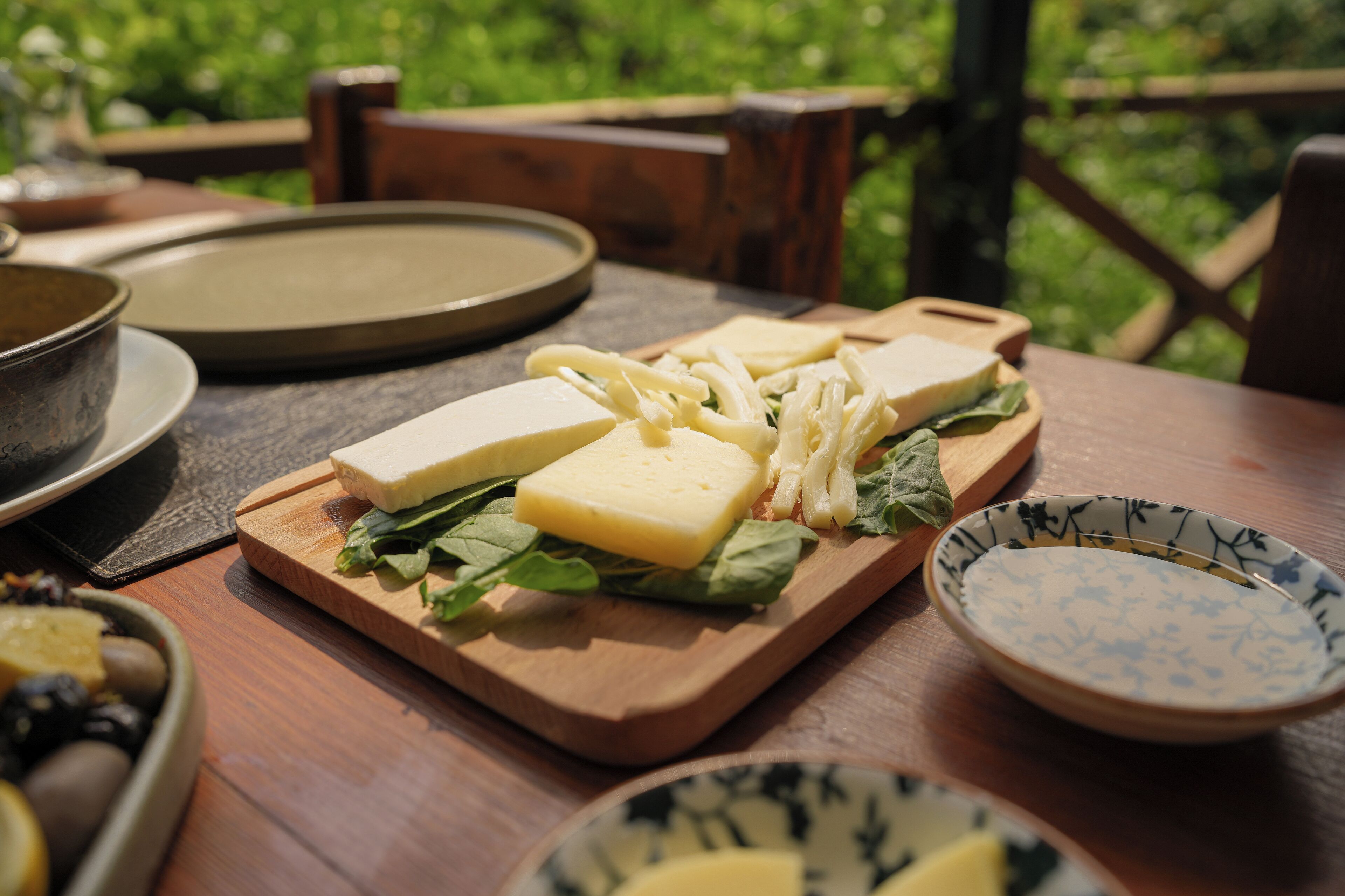 Ein Holztisch mit Schneidebrett, Käse und Salat, eine Oliven-Schale und ein dekorativer Teller.