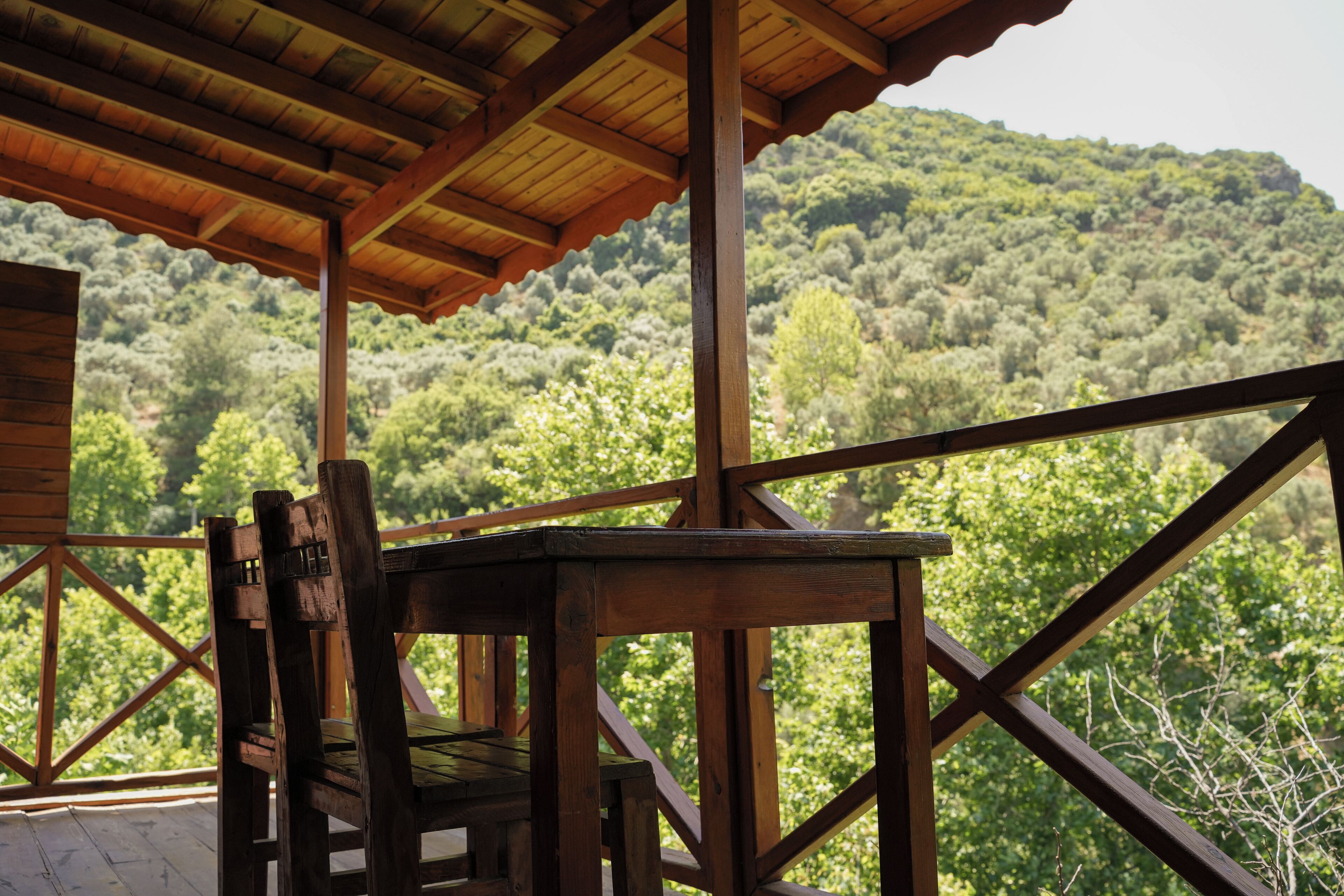 Una terraza de madera con una mesa y sillas, con vistas a una ladera boscosa.
