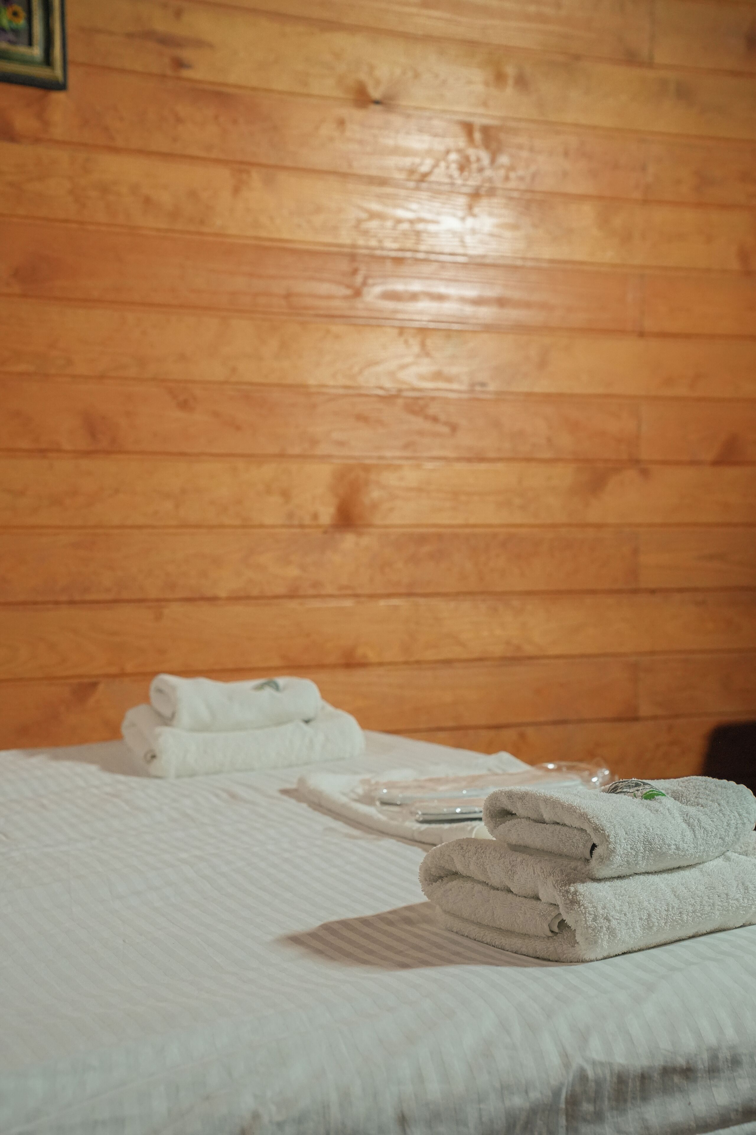 A neatly made bed with folded white towels and a glass of water on the wooden floor.