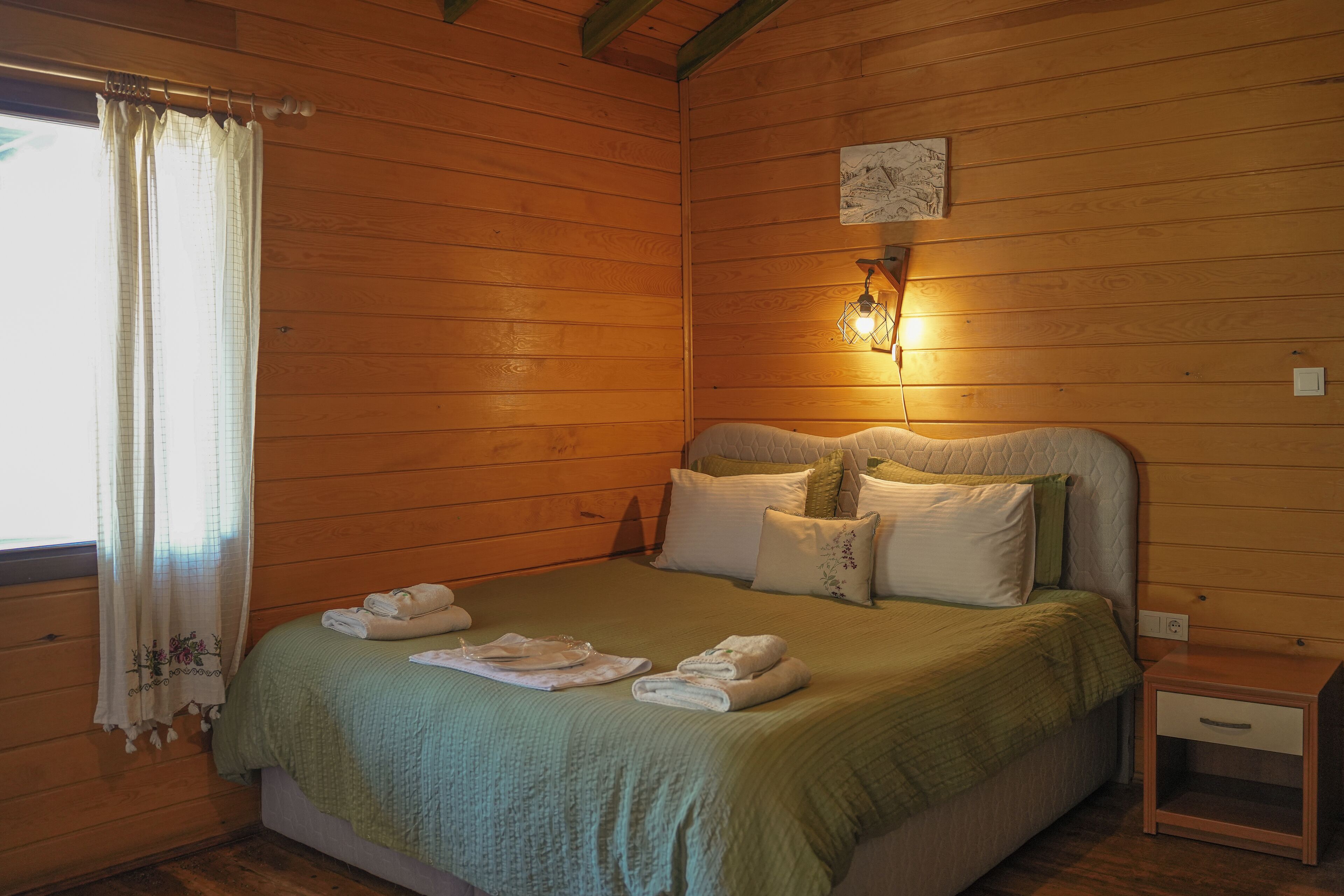 A wooden-paneled bedroom with a bed, pillows, a nightstand, and a wall-mounted light fixture.
