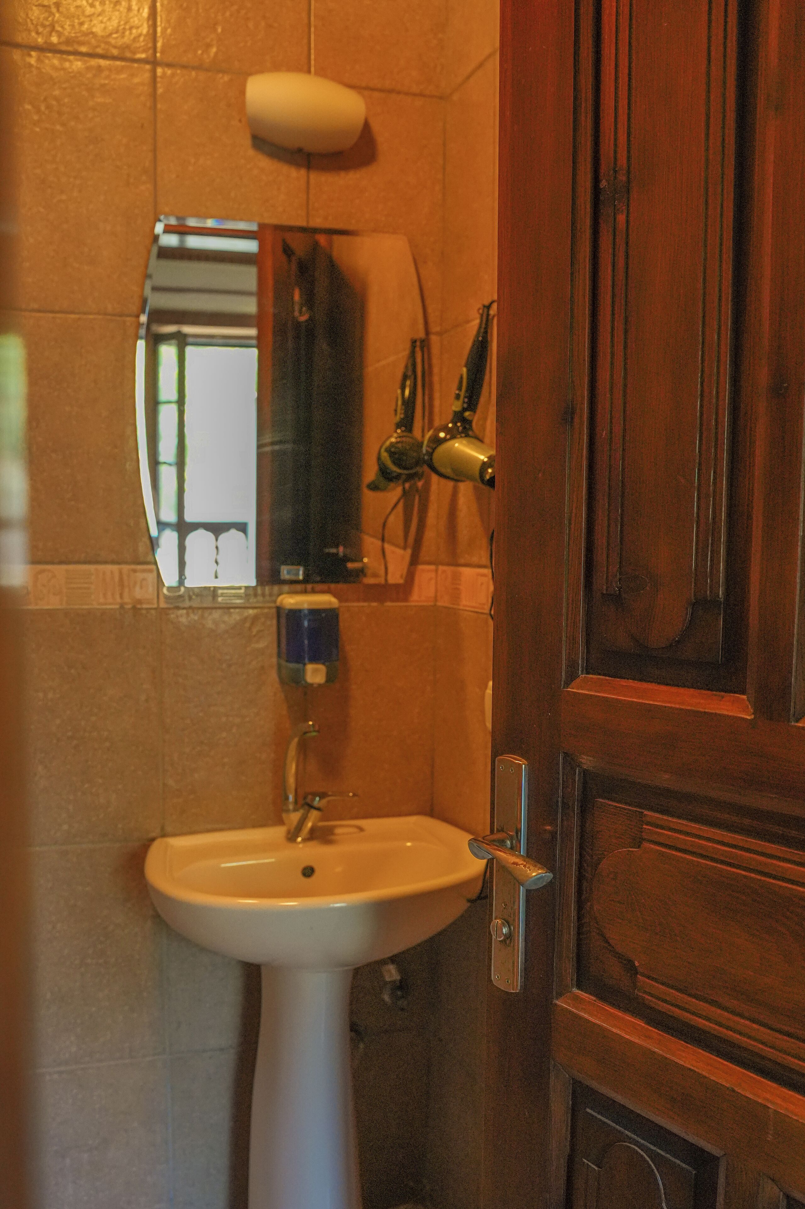 A bathroom with a pedestal sink, a mirror, a towel rack, and a wooden door.