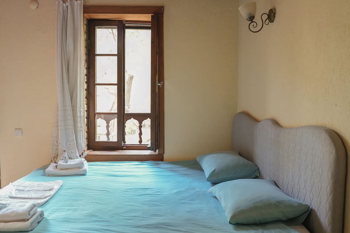 A room with a bed, a window with curtains, and a wall-mounted light fixture.