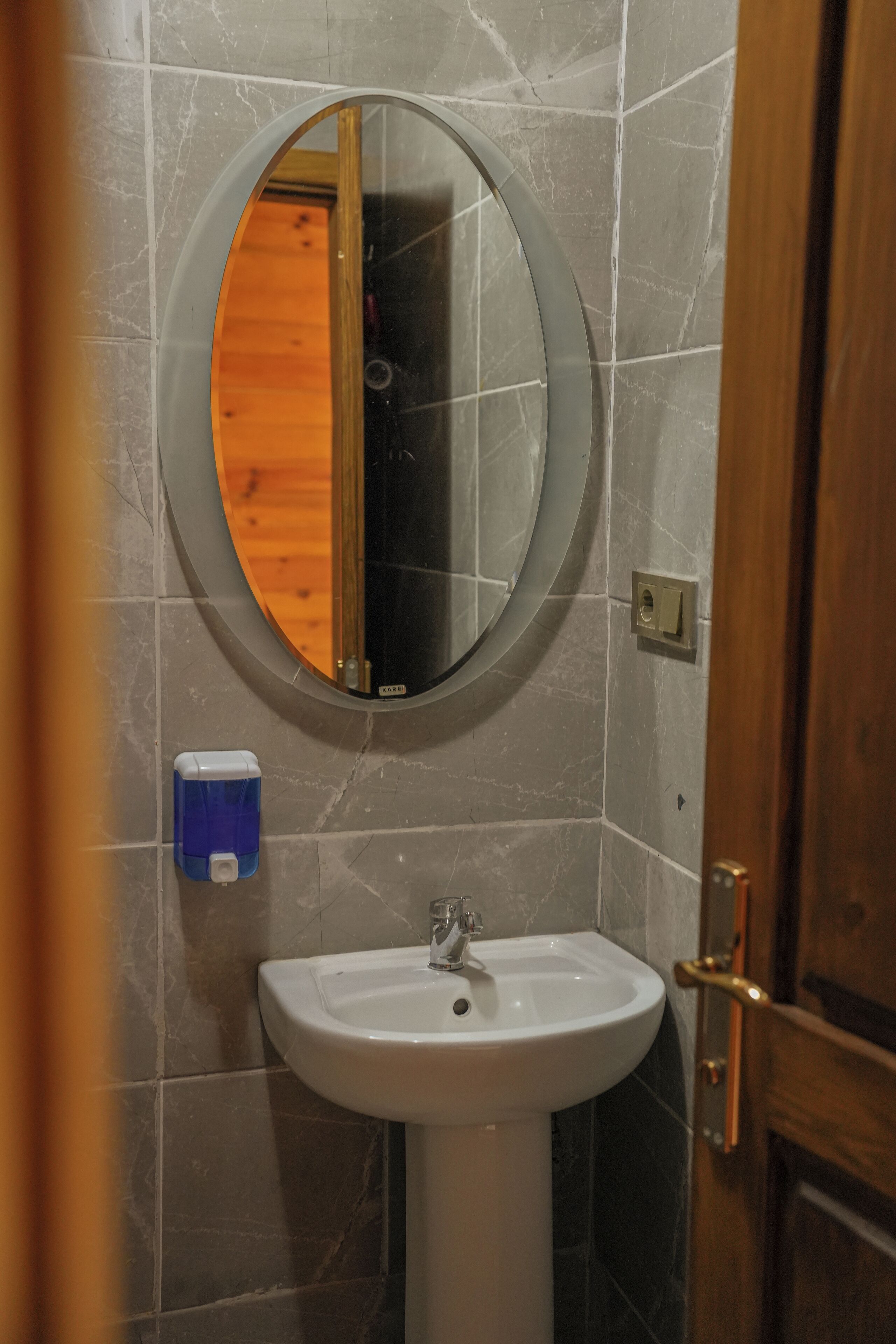 A bathroom with a round mirror, a white sink, and a soap dispenser.