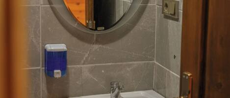 A bathroom with a round mirror, a white sink, and a soap dispenser.