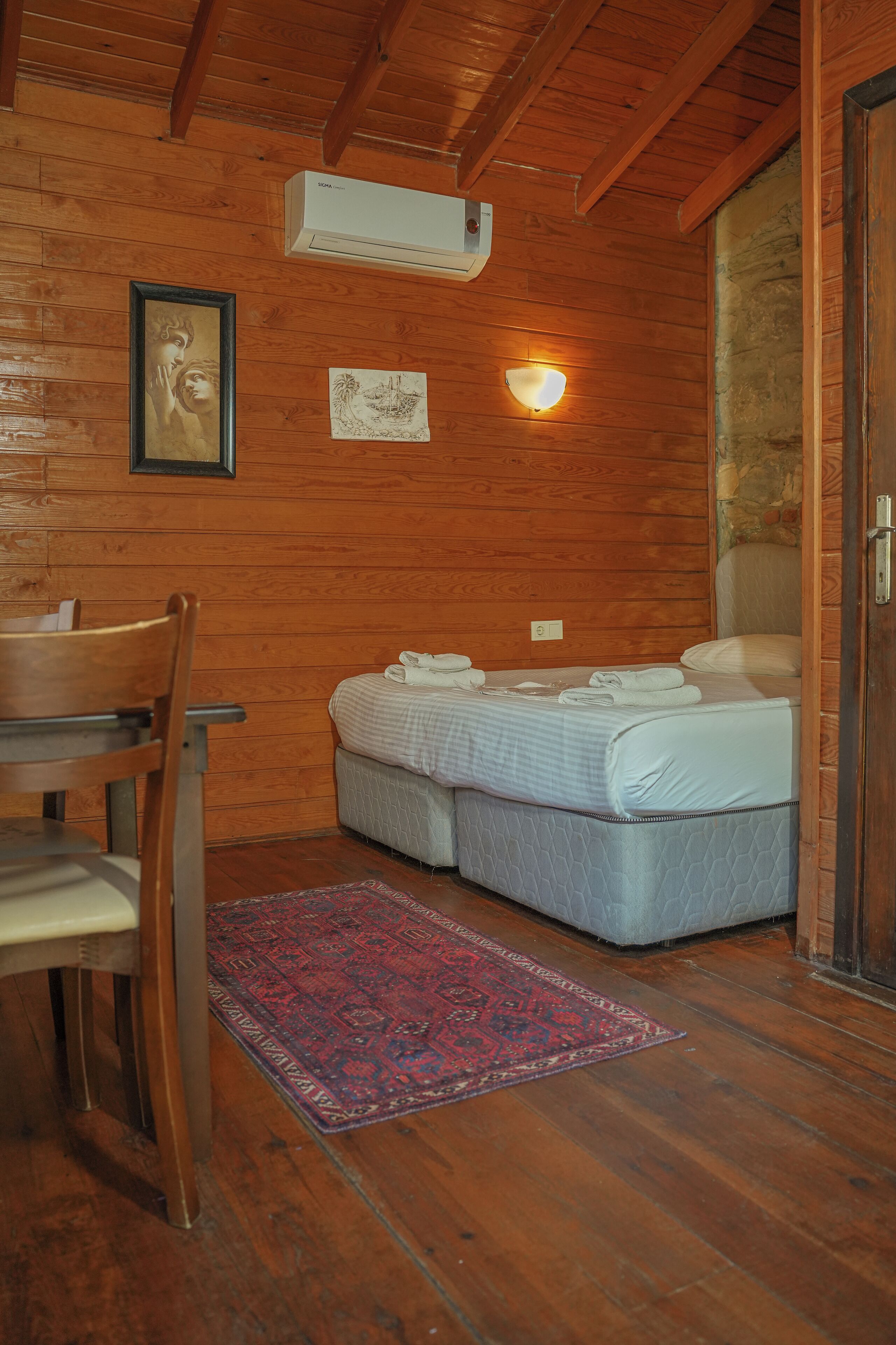 Habitación de cabaña de madera con cama, una silla, un tapete y un aire acondicionado montado en la pared.