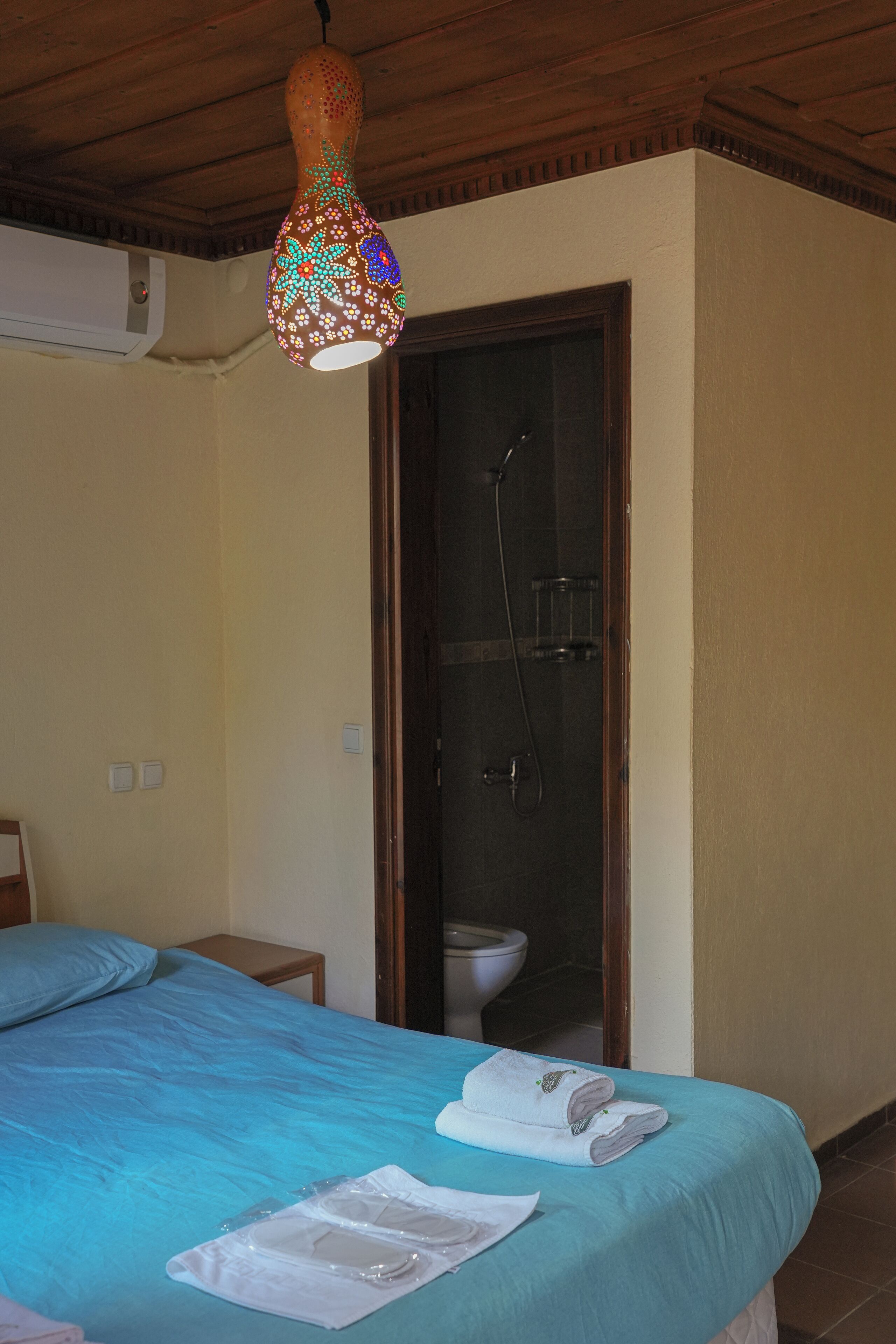 Ett hotellrum med en säng, en dusch och en dekorativ hängande lampa.