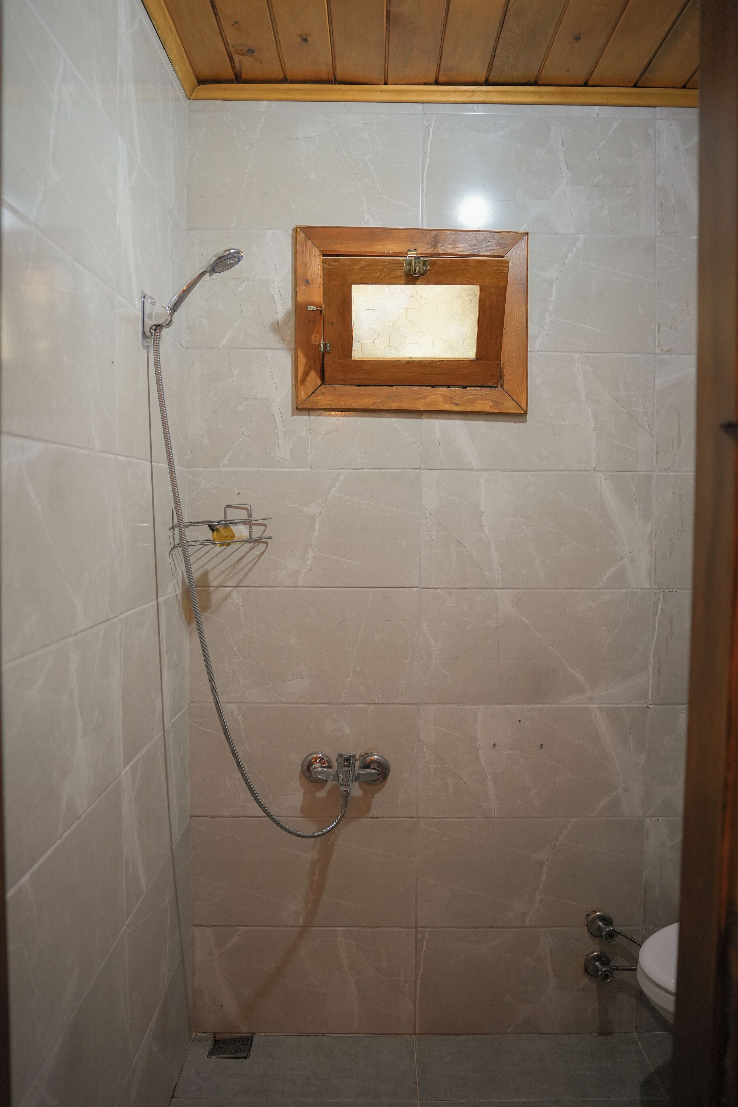 A small bathroom with a shower, a wooden-framed mirror, and a toilet.