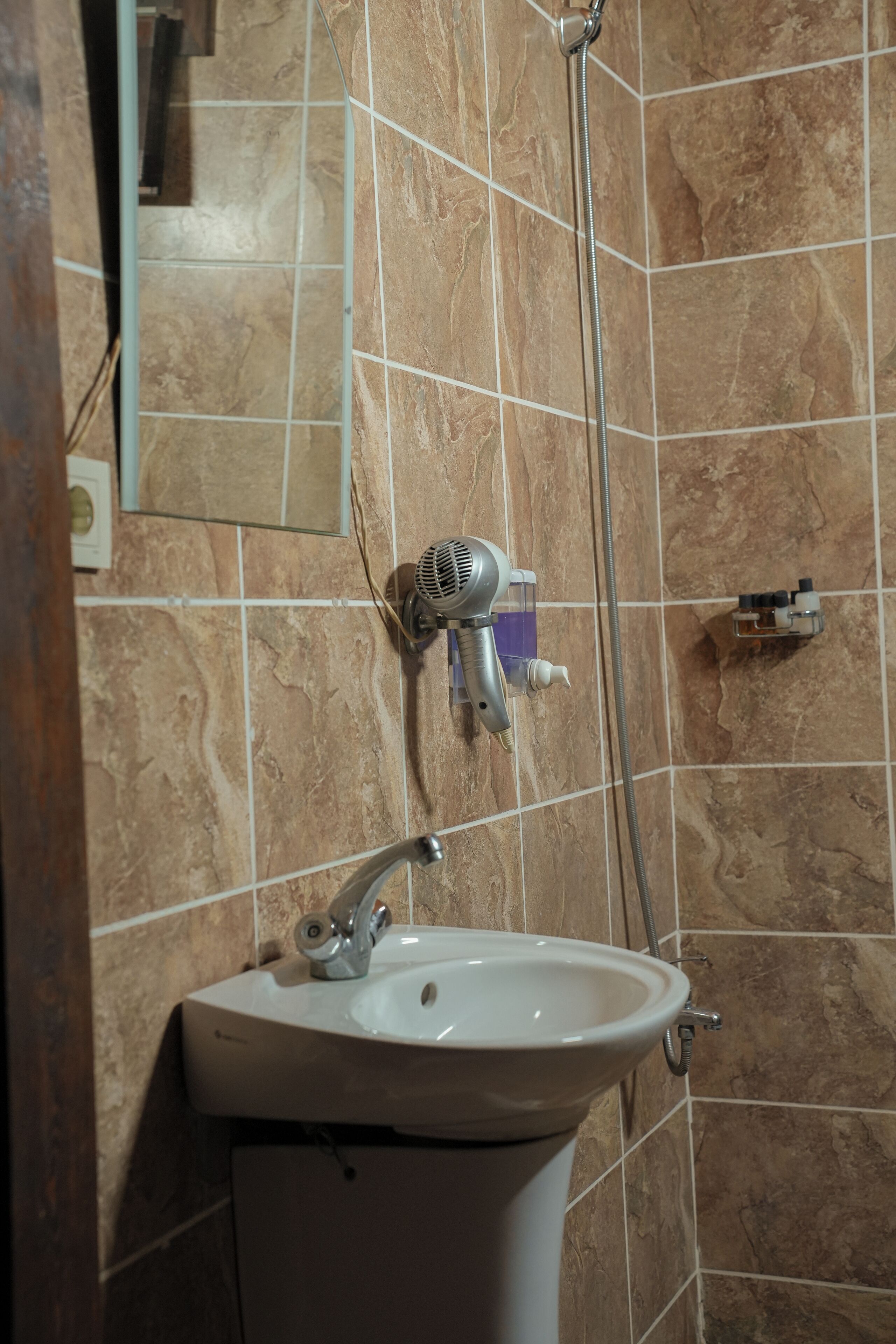 A bathroom with a sink, a handheld showerhead, and a hairdryer mounted on the wall.