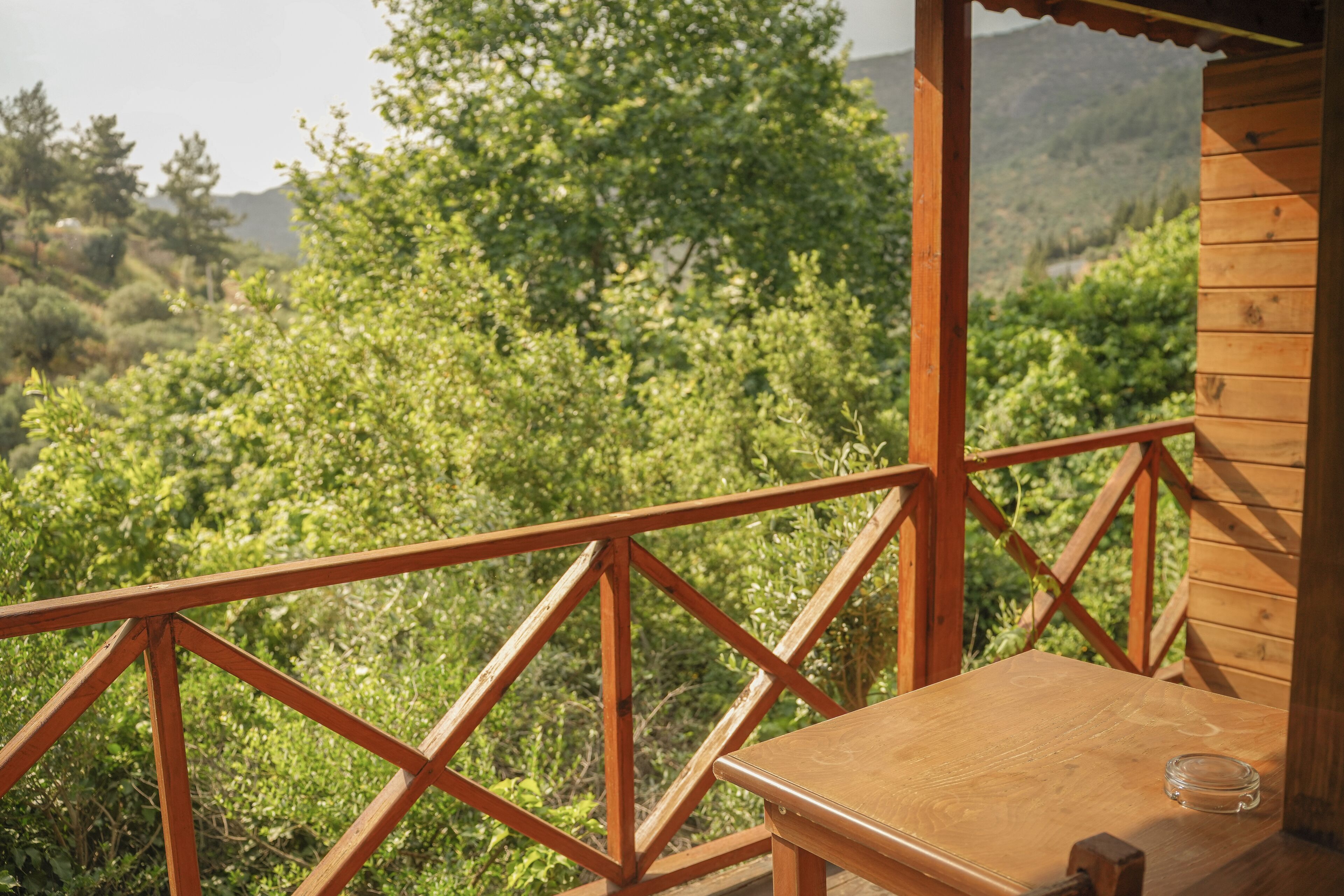 Eine Holzterrasse mit Tisch und einem Glas, mit Blick auf eine üppige grüne Landschaft.