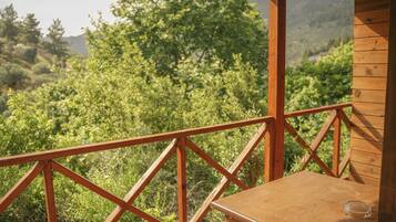 Eine Holzterrasse mit Tisch und einem Glas, mit Blick auf eine üppige grüne Landschaft.