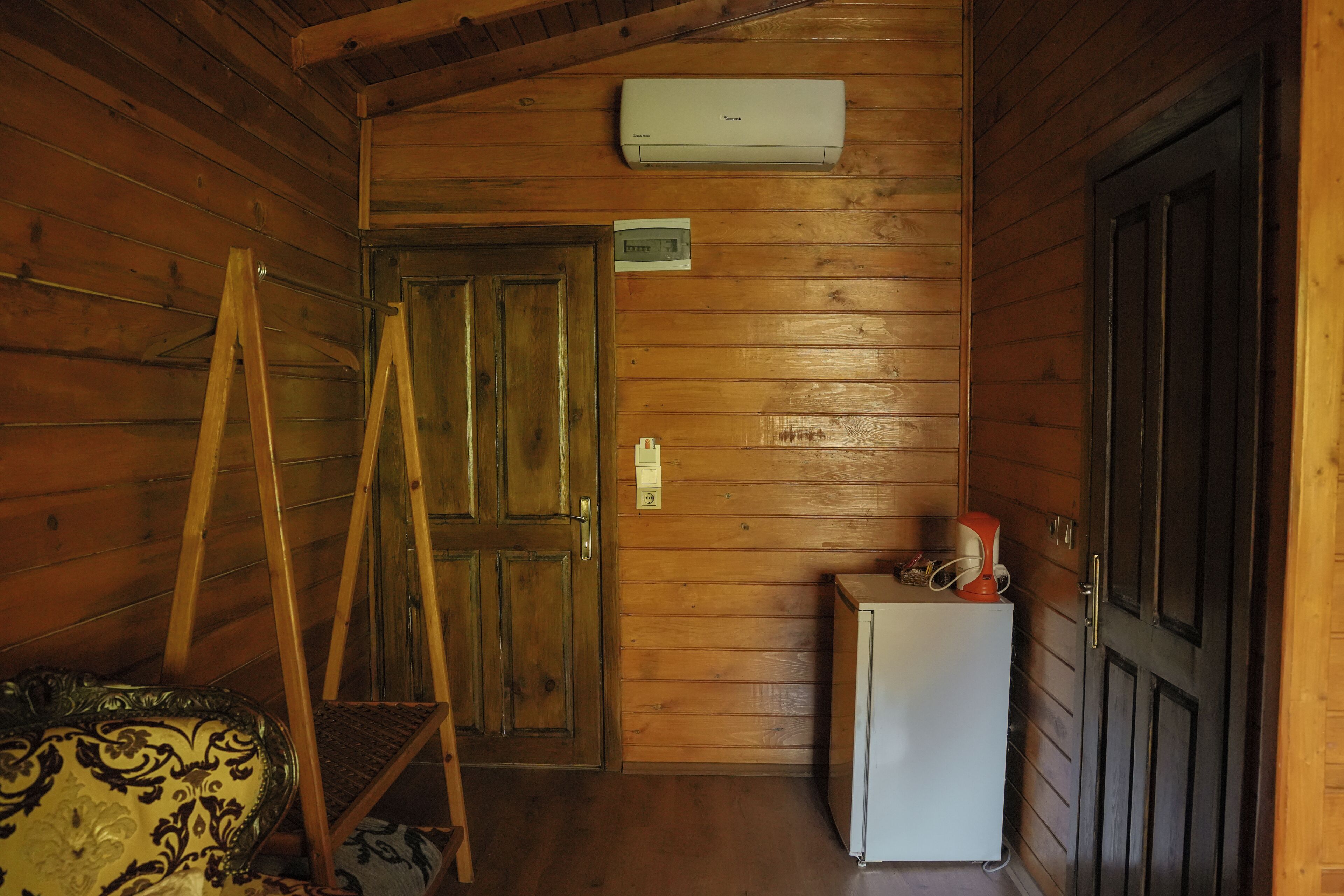 A wooden interior with a door, a small refrigerator, and an air conditioning unit on the wall.
