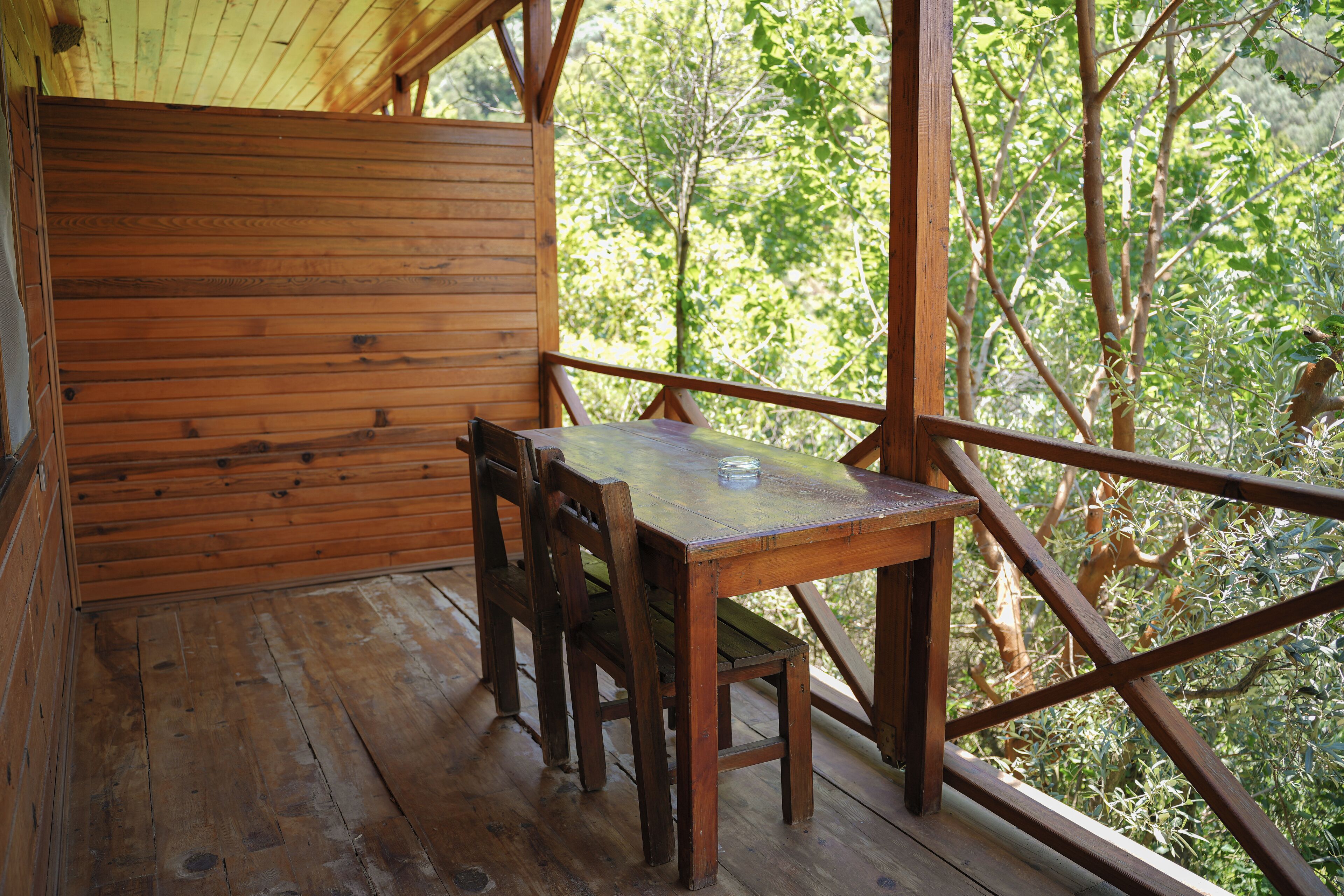 A wooden deck with a table and chairs, surrounded by a wooden railing, overlooking a forested area.