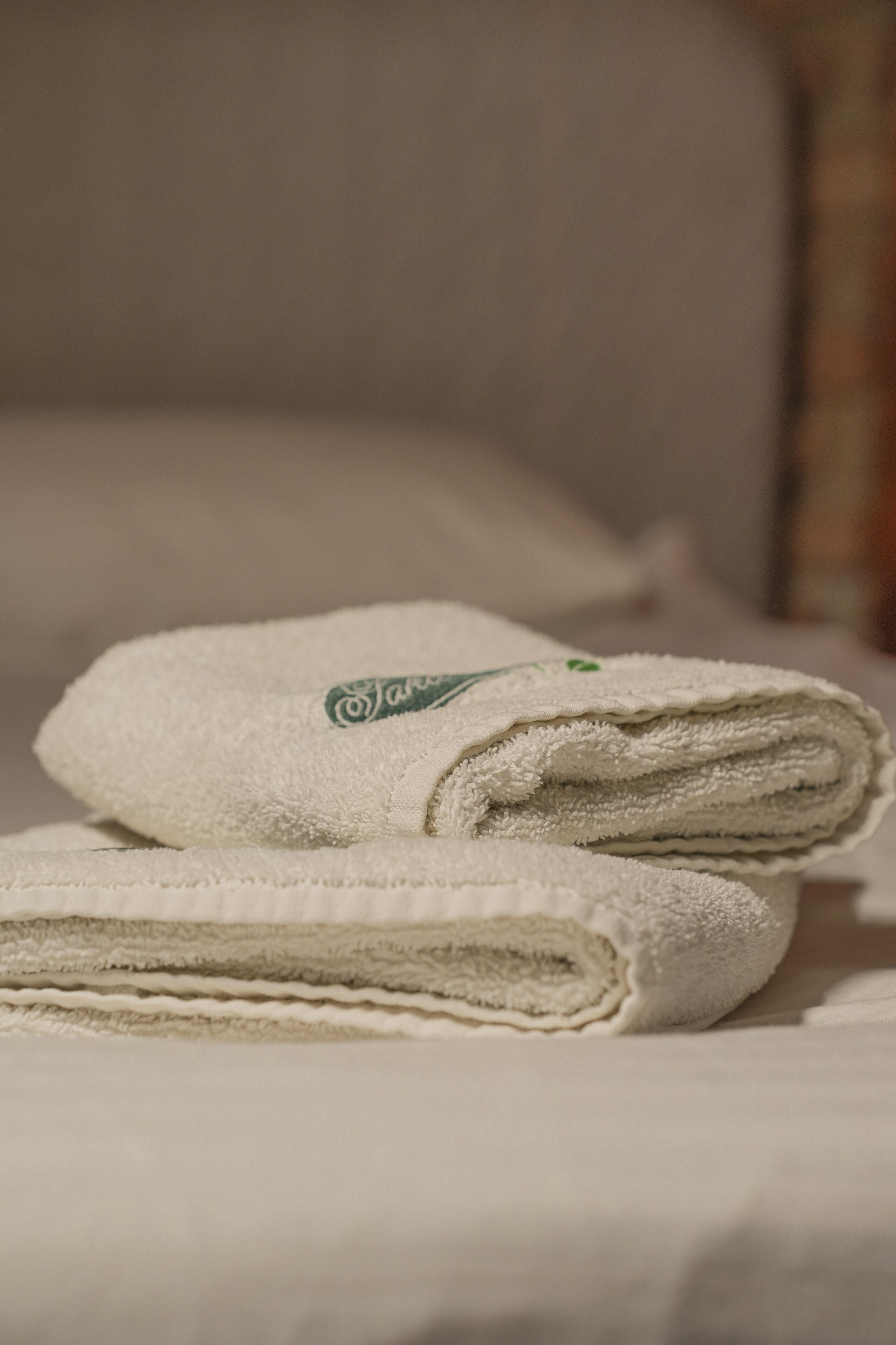 Two neatly folded towels with a logo on a bed.