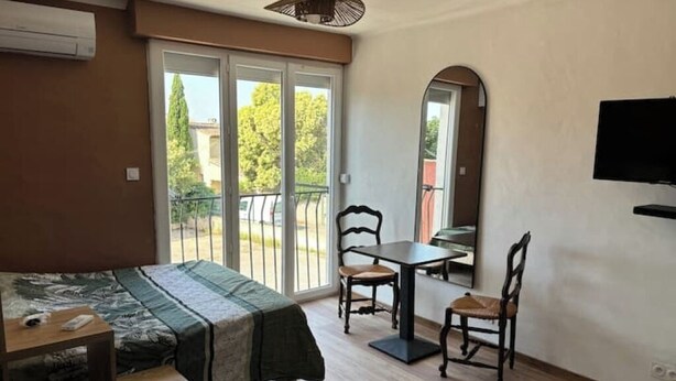 A room with a bed, a table, two chairs, a TV, and a sliding glass door leading to an outdoor area. - Cosy studio close to amenities + sea 5 minutes away (Fos-sur-Mer)