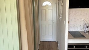 A narrow hallway with a white door at the end, a kitchen area with a microwave and a stove, and a tiled backsplash. - Cosy studio close to amenities + sea 5 minutes away (Fos-sur-Mer)