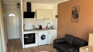 A compact kitchen with a washing machine, a built-in oven, and a black leather sofa in a living area. - Cosy studio close to amenities + sea 5 minutes away (Fos-sur-Mer)