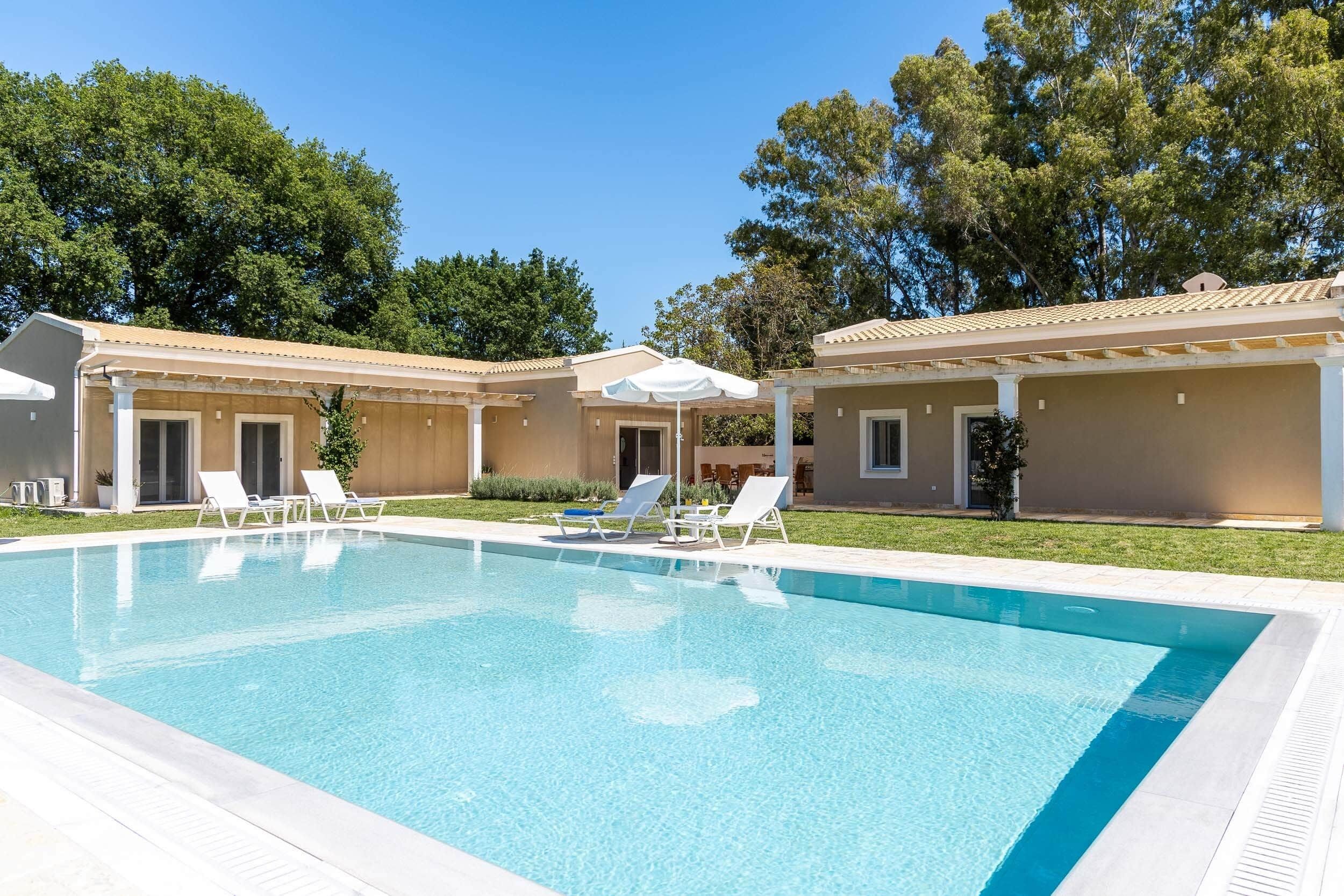 Uma piscina com espreguiçadeiras, um alpendre coberto e um edifício com telhado em azulejos.