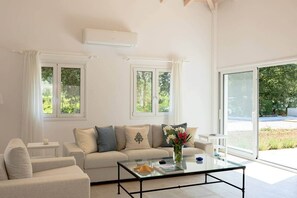 Un salon moderne avec un canapé, une table basse en verre et une vue sur la verdure à l’extérieur.
