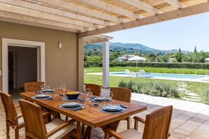 A wooden dining table set for six with chairs, a pool in the background, and a view of hills.