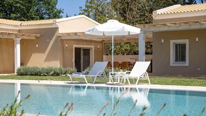 Ein Swimmingpool mit Liegestühlen und Sonnenschirm, umgeben von einem Gebäude mit einem Ziegeldach und einer Tür.
