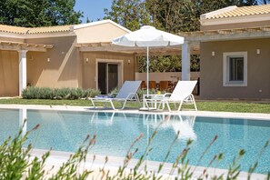 A swimming pool with lounge chairs and an umbrella, surrounded by a building with a tiled roof and a door.